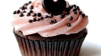 Chocolate cupcake with pink frosting swirl, topped with dark chocolate heart and sprinkled with mini chocolate chips on white background, close-up view.