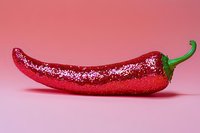 Red chili pepper covered with sparkly glitter on pink background, creative food art concept for festive culinary designs and holiday decorations.