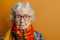 Senior Caucasian woman with white curly hair wearing vintage glasses, colorful patterned scarf and knitted sweater against vibrant orange background, expressing wisdom.