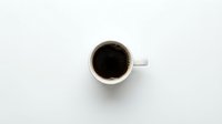 White ceramic coffee cup filled with black coffee on clean white background, top view flat lay composition for morning beverage and cafe concepts.