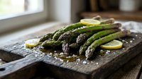 Fresh green asparagus spears with lemon slices and sea salt on rustic wooden cutting board, healthy organic vegetable cooking ingredient for spring recipes.