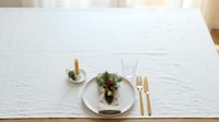 Elegant table setting with white plate, gold cutlery, and fresh greenery on white linen tablecloth for fine dining and event planning.