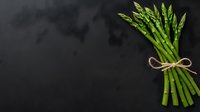 Fresh green asparagus bunch tied with twine rope on dark background. Minimalist food photography with copy space for menu design and healthy eating concept.