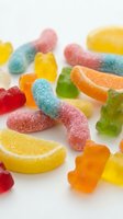 Colorful assorted gummy candies and jelly sweets scattered on white background. Sugar-coated sour worms, fruit slices and bear shapes for confectionery designs.
