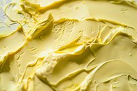 Creamy yellow butter texture with smooth swirls and waves, macro close up view showing rich dairy product surface detail for food and culinary backgrounds.