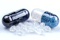Medical capsules filled with black and blue micro beads on white background with transparent gel pills, pharmaceutical concept for drug delivery and medicine.