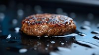 Juicy grilled beef burger patty with coarse salt and pepper on dark background, macro shot with selective focus and water drops for food photography.