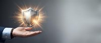 Shield with glowing light effect held in open palm of businessman wearing suit jacket, symbolizing protection, security, and trust for business concepts.
