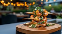 Grilled shrimp skewers garnished with fresh herbs and spices on wooden serving board, bokeh lights creating warm ambiance in outdoor restaurant setting.