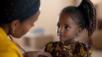 African American mother and daughter share tender moment at home, young girl wearing traditional patterned dress listens attentively as parent speaks with care.