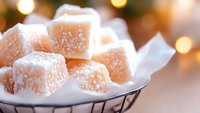 Sweet pink Turkish delight cubes dusted with powdered sugar in metal basket against soft bokeh lights background, creating cozy festive atmosphere.