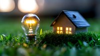 Glowing light bulb and miniature house on grass at dusk, creating cozy atmosphere. Concept of eco-friendly home, energy efficiency and sustainable living solutions.