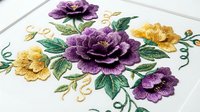 Purple and yellow embroidered flowers with green leaves and gold swirls on white fabric. Decorative floral needlework design for textile art, home decor, and craft projects.