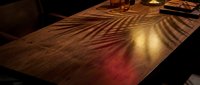 Wooden table surface with warm golden and red light casting striped shadows, creating dramatic lighting effects for interior design and ambiance concepts.