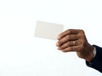 Male hand with dark skin tone holding blank white card, wearing gold wedding band and navy sleeve, isolated on white background for business card mockup, presentation, or corporate design use.
