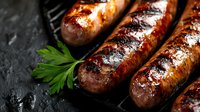 Grilled sausages with grill marks and charred surface on dark background, garnished with fresh parsley leaf. Close-up view of juicy bratwurst.
