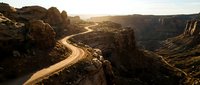 Winding river curves through dramatic rocky canyon landscape with golden sunlight illuminating towering cliff formations and desert terrain, suitable for travel, nature, and environmental design projects.