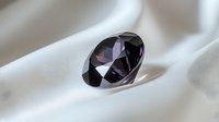 Dark purple diamond gemstone on soft white silk fabric background, luxury jewelry and precious stone close-up with selective focus and reflective surface.