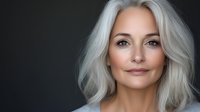 Professional mature Caucasian woman with silver gray hair and natural makeup against dark background for business and lifestyle concepts.
