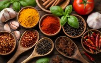 Colorful spices and herbs in wooden bowls with fresh basil, tomatoes, garlic and cinnamon sticks on rustic table for cooking and seasoning dishes.