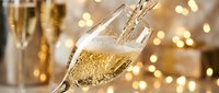 Champagne pouring into glass with festive bokeh lights and bottles in background, celebration and toast moment.