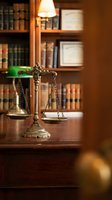 Brass scales of justice on wooden desk in law office with books and warm lighting for legal services and attorney consultation.