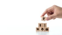 Hand placing wooden block with house icon on stack of cubes with real estate symbols for property investment and home buying concepts.