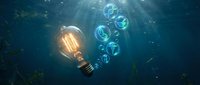 Glowing light bulb underwater with floating bubbles in deep blue ocean water creating magical illumination effect for creative energy concepts.