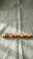 Wooden letter blocks spelling PRACTICE arranged on natural linen fabric background for mindfulness and skill development concepts.