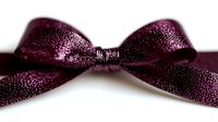 Elegant burgundy satin bow with sparkly glitter pattern isolated on white background, suitable for gift wrapping, holiday decorations and craft projects.