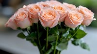 Delicate peach-colored roses with fresh green leaves arranged in elegant bouquet against soft blurred background, showcasing romantic floral composition for wedding and events.