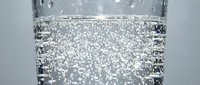 Sparkling water in a clear glass with rising bubbles, close-up macro shot on a light gray background, refreshing drink concept.