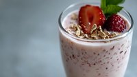 Fresh strawberry smoothie topped with granola, mint leaves and berries in glass on gray background. Healthy breakfast protein shake with pink creamy texture.