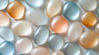 Luminous pastel glass beads in soft peach, blue and white tones arranged in rows creating gentle shadows and reflections on light background.