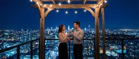 Young couple enjoying romantic evening on rooftop terrace with city skyline view and string lights creating intimate atmosphere for date night.