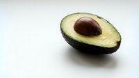 Fresh ripe avocado half with pit on clean white background isolated for healthy cooking and nutrition design projects.