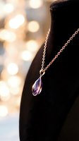 Silver chain necklace with amethyst teardrop pendant displayed on black velvet bust form against warm bokeh background for jewelry retail and luxury accessory marketing.