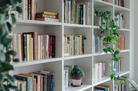 Modern white bookshelf with diverse collection of books and decorative green plants creating cozy home library atmosphere, perfect for interior design and lifestyle content.