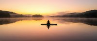 Silhouette of kayaker paddling on calm lake at sunrise with golden sky reflection, peaceful morning water sport adventure creating perfect mirror symmetry.