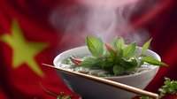Steaming Asian soup bowl with fresh herbs and chopsticks against red background with Chinese flag star, atmospheric food photography for restaurant menu.