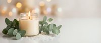 Spa wellness scene with burning candle, eucalyptus leaves and sea salt on white surface with golden bokeh lights creating relaxing atmosphere.