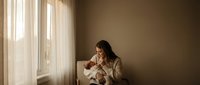Young woman in cozy sweater sitting by window with warm natural light, peaceful morning moment for wellness and self-care content.