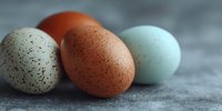 Three colorful speckled eggs in natural brown, cream and pale blue tones arranged on textured surface for Easter, cooking and farm fresh concepts.