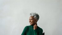 Senior woman with gray hair wearing dark green shirt, smiling while looking away against white background, suitable for healthcare, wellness, lifestyle and portrait design projects.