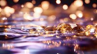 Glowing golden water drops on reflective purple surface with magical bokeh lights in background creating dreamy atmospheric composition.