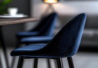 Modern navy blue velvet dining chair with black metal legs in contemporary interior setting, soft focus background shows minimalist restaurant or cafe atmosphere.