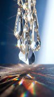 Hanging crystal chandelier pendants refracting rainbow light on dark surface, sparkling prism reflections against deep blue background.