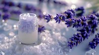 Fresh lavender sprigs beside small glass jar with bath salts and moisturizer on crystal surface in soft morning light, creating spa wellness atmosphere.