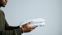 Middle-aged man with medium skin tone holding folded white towels or linens against neutral background for laundry, household, and domestic care concepts.