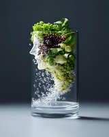 Fresh vegetables and fruits submerged in sparkling water creating profile silhouette in clear glass, dramatic lighting against dark background for healthy lifestyle concept.